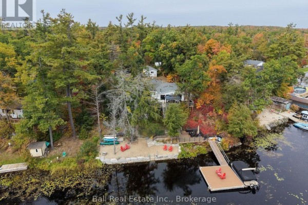 The waterfront home at 20 Fire Route 93 sits on a wooded lot with a dock and sandy shore. - 20 Fire Route 93, Trent Lakes