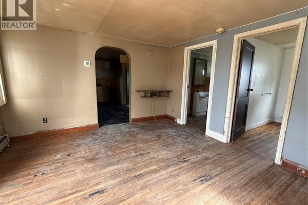 Living room with light brown walls, hardwood floors, an archway to the kitchen, and doorways to bathroom and bedroom. - 20 First Street, Wallaceburg