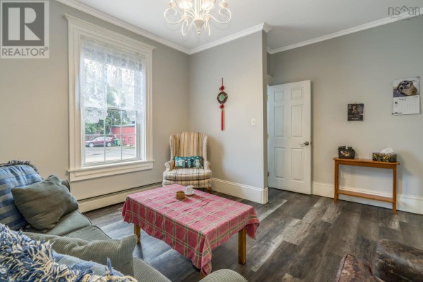 Living room with a sofa, armchair, coffee table, window with lace curtains, and a door leading out. - 20 Gray Street, Windsor