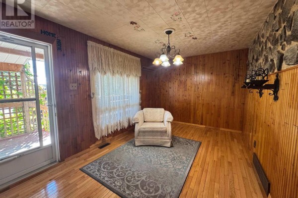 Interior dining area with wood-paneled walls, a floral patterned ceiling, and a single armchair on a rug. - 20 Heron Drive, Manitouwadge