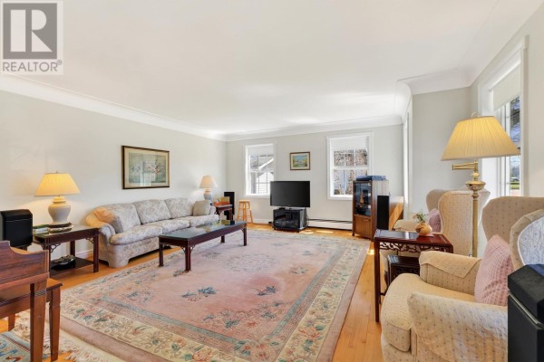 A living room with a large pink floral rug, light blue walls, a sofa, armchairs, and a television. - 20 Johnson Avenue, Charlottetown
