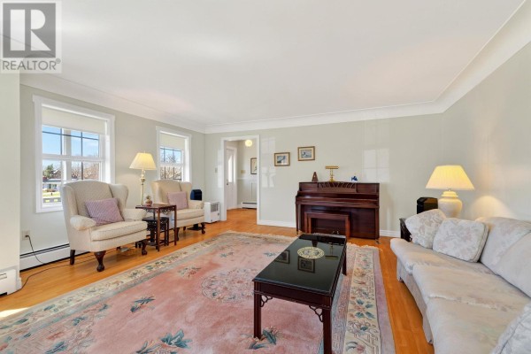 A living room featuring a dark wood upright piano, sofas, armchairs, a large floral rug, and wood floors. - 20 Johnson Avenue, Charlottetown
