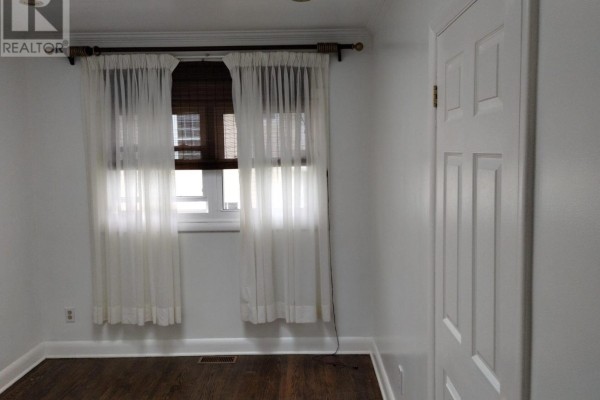 Bedroom with white walls, sheer white curtains, a brown rug, and a white paneled door on the right. - 20 Johnson Street, Prince Edward County