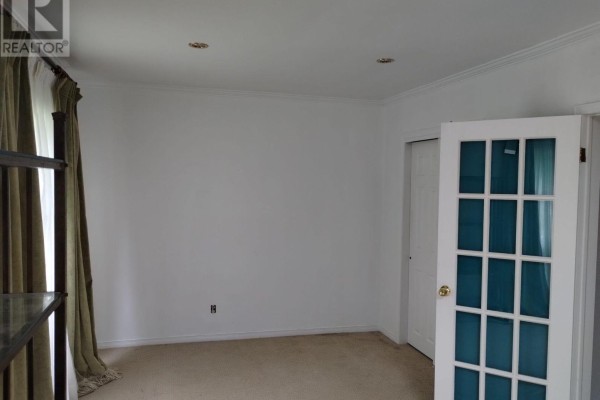 Empty room with beige carpet, white walls, a glass-paneled door, and a large window with green curtains. - 20 Johnson Street, Prince Edward County