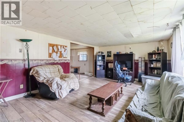 Living room with wood-paneled walls, patterned armchair, and a covered sofa. - 20 Mardon Avenue, Port Dover