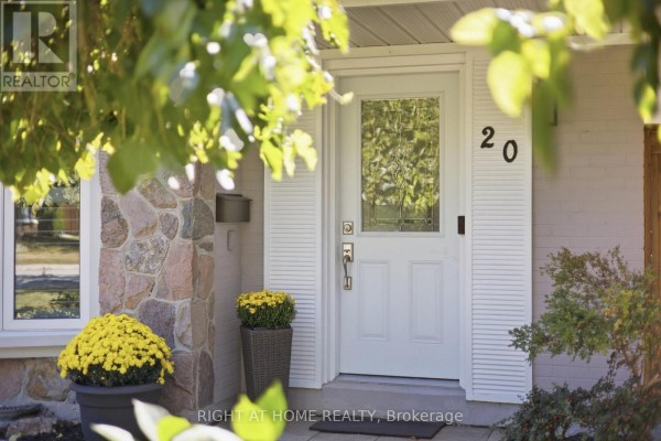 Front door with glass insert, flanked by stone and white siding, with potted mums. - 20 Mono Court, Brampton