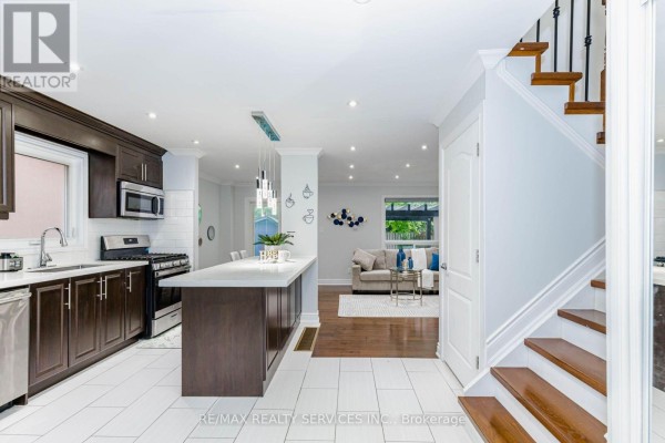 Kitchen with dark wood cabinets, stainless steel appliances, white tiled backsplash, and island. - 20 Murdoch Drive, Brampton