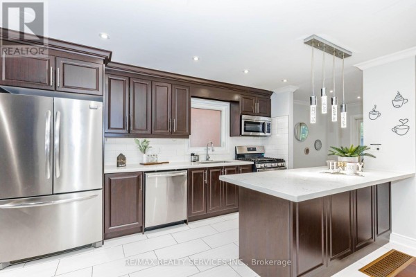 Modern kitchen with dark wood cabinets, stainless steel refrigerator, oven, dishwasher, and island. - 20 Murdoch Drive, Brampton