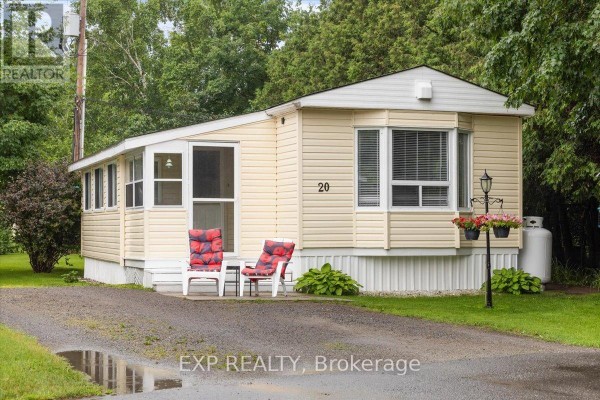 A beige mobile home with two red chairs on the porch in front of the entrance. - 20 Pinewood Avenue, Beckwith