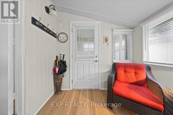 Sunroom with a wicker chair, coat rack, clock, and door leading outside. - 20 Pinewood Avenue, Beckwith