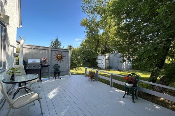 A light grey wooden deck with outdoor furniture, a grill, and a decorative sun accent. - 20 Poplar Street, Pine Falls