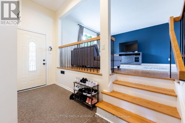 Interior view of a home entryway with a white door, carpet, shoe rack, wooden stairs, and a living room with blue accent wall. - 20 Sanderson Crescent, Richmond Hill