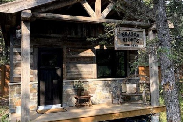 Outdoor patio area with fire pit, seating, string lights, and wooden walkway over a pond. - 20 Spruce Avenue, Bragg Creek