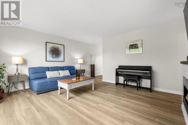 Living room with blue sofa, coffee table, digital piano, lamps, and light wood flooring. - 20 Stratford Drive, Cole Harbour