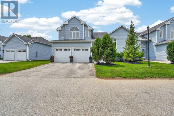 Exterior townhouse view with blue siding, double garage, green lawn, and evergreen trees. - 20 Sundial Court, Collingwood