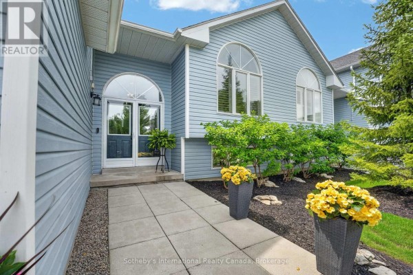 Close-up of a townhouse entrance with a glass door, stone walkway, and potted yellow flowers. - 20 Sundial Court, Collingwood
