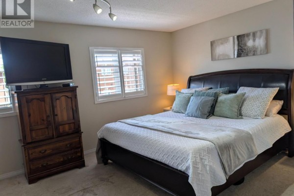 Bedroom with a king-size bed, dark wood dresser with TV, and light gray walls. - 20 Thorp Crescent, Ajax