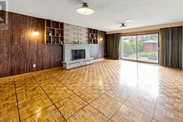 Family room with wood-paneled walls, stone fireplace, parquet flooring, and sliding glass doors. - 20 Torrens Avenue, Toronto