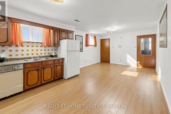 Basement kitchen with wood cabinets, white refrigerator, patterned backsplash, and light wood flooring. - 20 Torrens Avenue, Toronto