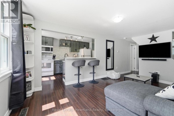 Living room with gray sectional sofa, coffee table, and open concept kitchen with bar stools. - 20 William Street S, Central Huron