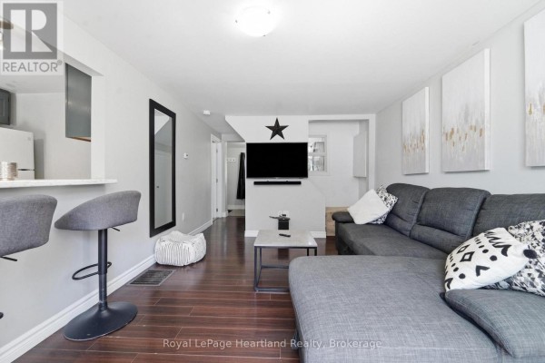 Living area with gray sectional sofa, wall-mounted television, and view of the kitchen area. - 20 William Street S, Central Huron