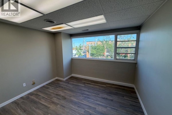 Office room with grey walls, grey vinyl flooring, and a large horizontal window overlooking the street. - 200, 10009 101 Avenue, Grande Prairie