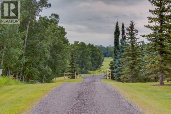 Gravel driveway leading to a black metal gate with a wooded landscape. - 200, 200042 198 Avenue W, Rural Foothills County