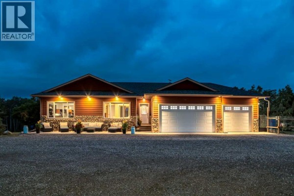 House exterior at dusk with exterior lights illuminating the red siding and garage doors. - 200, 200042 198 Avenue W, Rural Foothills County