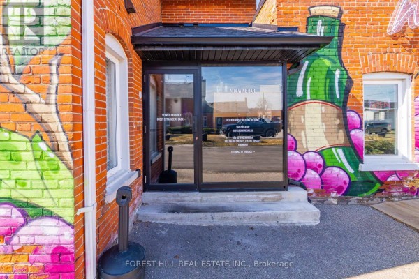 Exterior entrance with glass doors, brick walls, and colorful graffiti art of a wine bottle. - 200 - 151 Queen Street S, Mississauga
