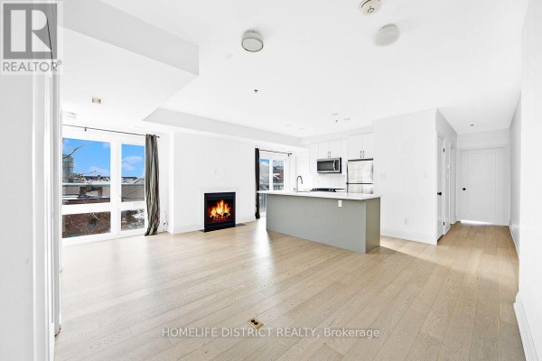 Living area with fireplace, large windows, and an open-concept kitchen with an island. - 200 - 243 Niagara Street, Toronto