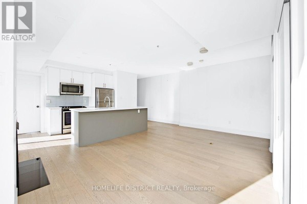 Open-concept living space and kitchen with light wood floors and white walls. - 200 - 243 Niagara Street, Toronto