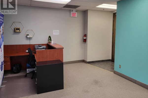 Interior reception area with a wooden desk, beige carpet, and light blue wall. - 200 - 3100 Steeles Avenue W, Vaughan