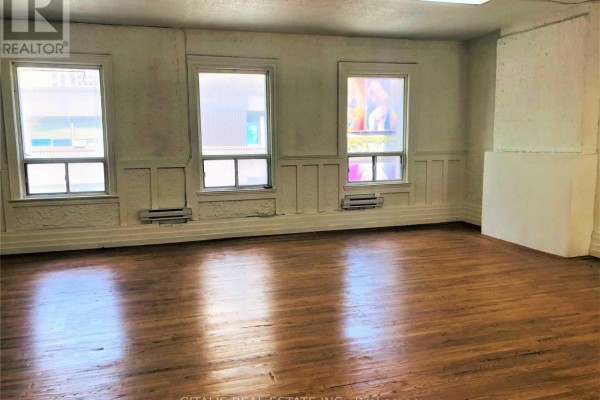 Interior room with hardwood floors and three large windows offering a view of the street. - 200 - 750 Yonge Street, Toronto