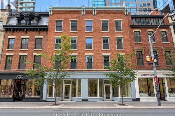 Exterior view of a brick commercial building with large windows and storefronts. - 200 - 83 King Street E, Toronto