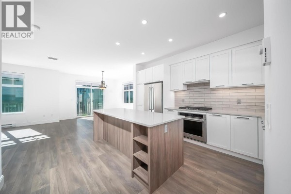 Modern kitchen with white cabinets, large island, and stainless steel appliances. - 200 1290 Mitchell Street, Coquitlam