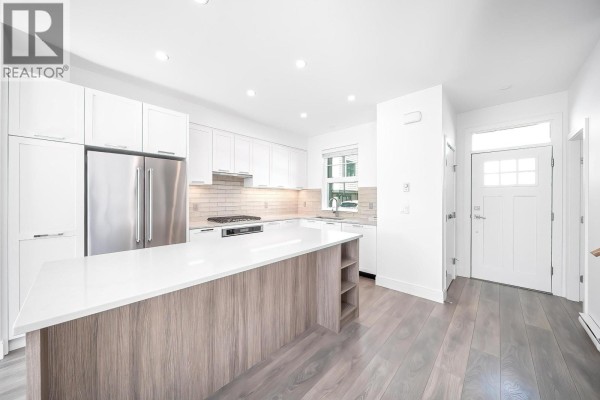 Open concept kitchen and entryway with white cabinets, island, and front door. - 200 1290 Mitchell Street, Coquitlam
