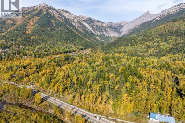 Aerial perspective of a mountain road with a river and forested slopes leading to jagged peaks. - 200 Canyon Trail, Fernie