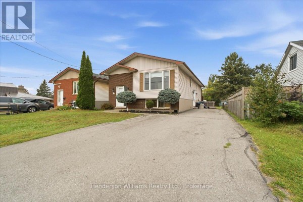 Side exterior view of a brick and vinyl siding house with a paved driveway and wooden fence. - 200 College Street E, Belleville