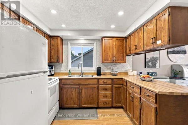 Kitchen with white appliances, wooden cabinets, L-shaped countertop, and a sink under the window. - 200 College Street E, Belleville