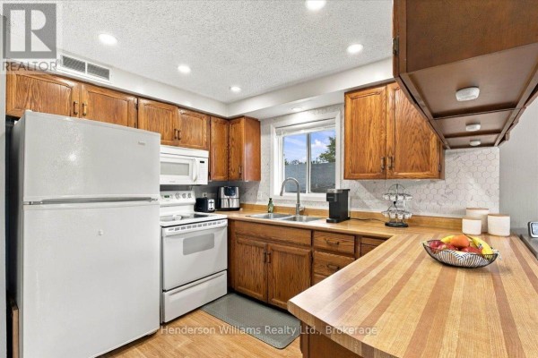 Kitchen with white appliances, wooden cabinets, L-shaped butcher block and laminate countertops, and a window view. - 200 College Street E, Belleville