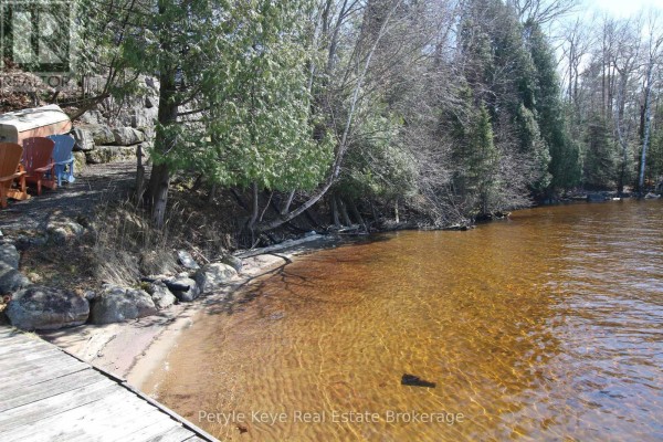 Concrete shoreline edge with rocks and trees leading to a calm lake. - 200 Edgemere Road, Huntsville