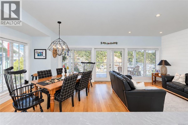 Dining area with a wooden table and checkered chairs, adjacent to a living room and patio doors. - 200 Marina Way, Sooke