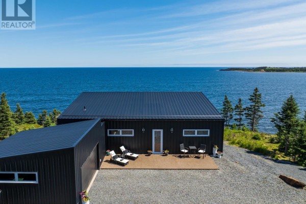 Exterior of a black house with a deck, lounge chairs, and table facing the blue ocean. - 200 Middle Road, Kingsburg