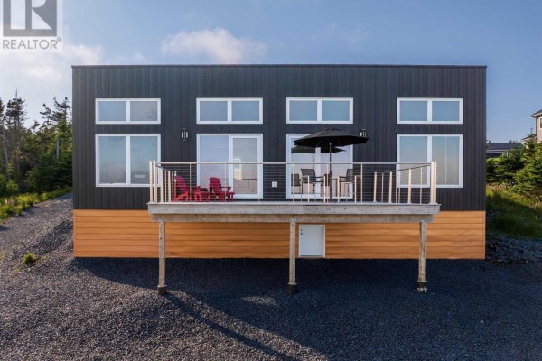 Front exterior of a black house with a wooden deck, red chairs, and large windows. - 200 Middle Road, Kingsburg