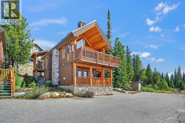 Side exterior view of a chalet with evergreen trees and a bright blue sky. - 200 Moonshine Crescent Unit# 11, Big White