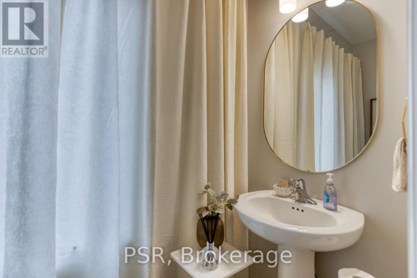 Bathroom vanity with a white pedestal sink, gold-framed oval mirror, and cream-colored shower curtain. - 200 Rivergreen Crescent, Cambridge