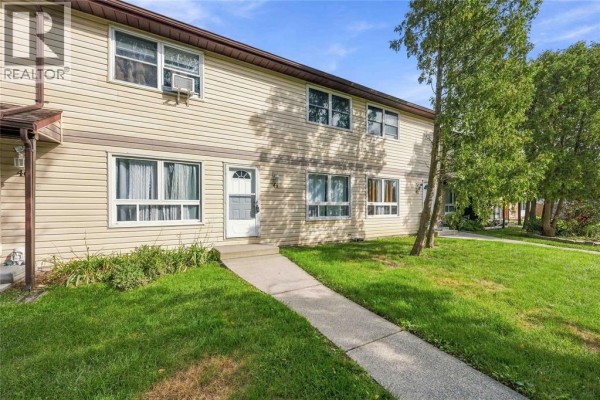 Exterior view of a light yellow townhouse with green grass and trees. - 200 St Clair Boulevard Unit# 44, St Clair
