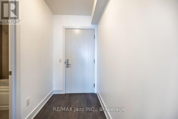 An empty apartment hallway with white walls, dark wood floors, and a white front door. - 2001 - 2550 Simcoe Street N, Oshawa