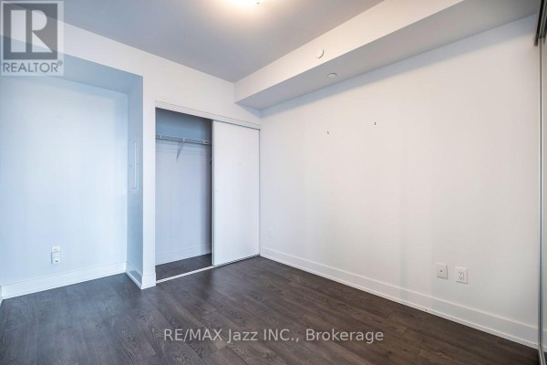 An unfurnished bedroom with white walls, dark wood floors, and a large sliding door closet. - 2001 - 2550 Simcoe Street N, Oshawa