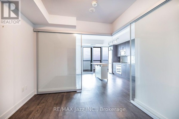 A spacious apartment living area with dark wood floors and frosted glass sliding doors. - 2001 - 2550 Simcoe Street N, Oshawa
